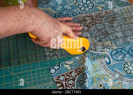 Closeup of a woman`s hands using a rotary cutter to cut quilting fabric Stock Photo